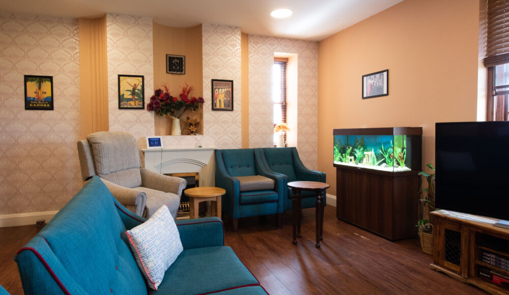 A stylish living room with a blue sofa and armchairs, a colorful fish tank and a TV, offering a serene space for entertainment and leisure activities.