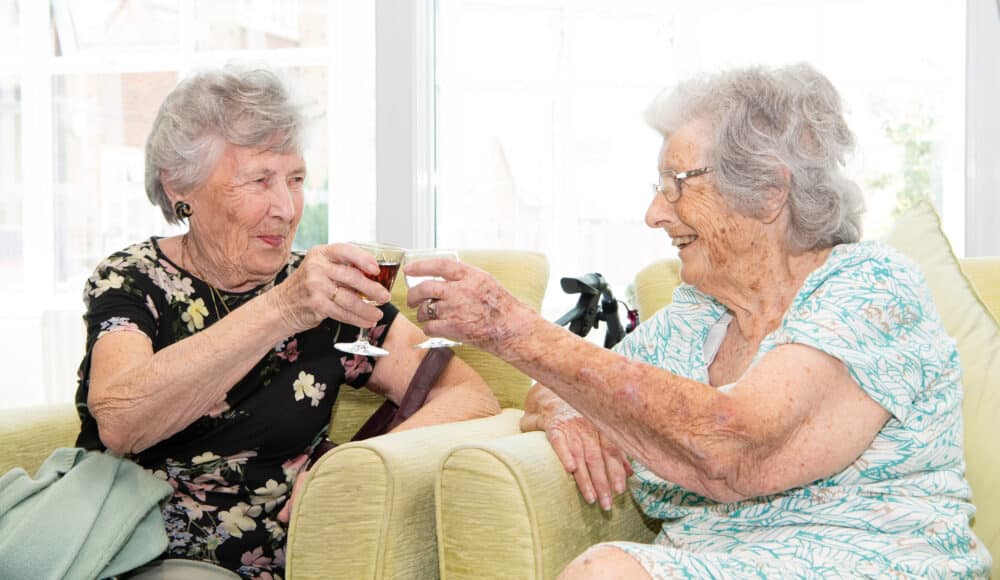 Two female residents enjoying a joyful moment together while sipping wine and sharing laughter.