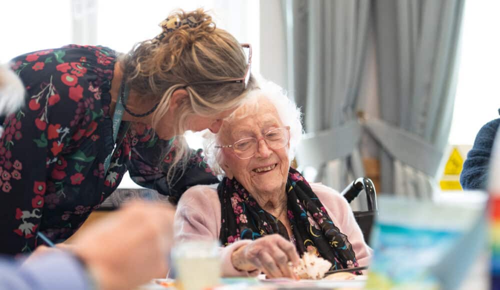 A female staff member supports a female resident as she works on her cake.