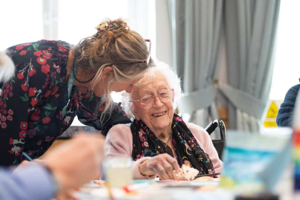 A female staff member supports a female resident as she works on her cake.
