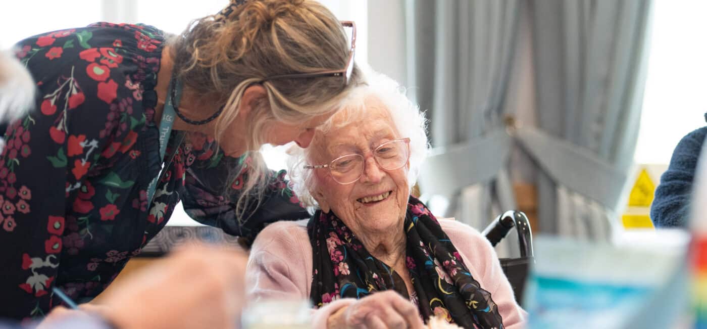A female staff member supports a female resident as she works on her cake.