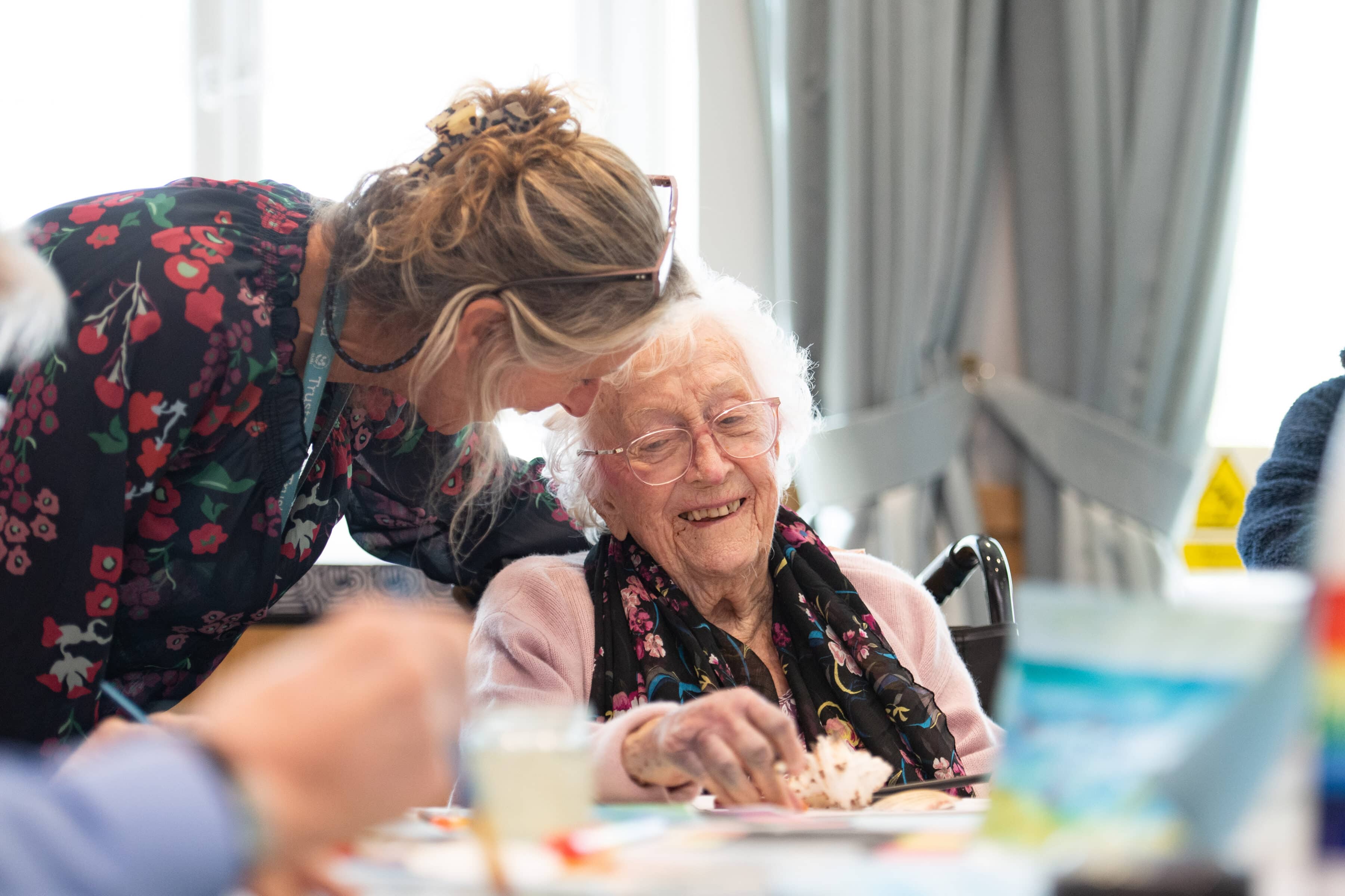 A female staff member supports a female resident as she works on her cake.