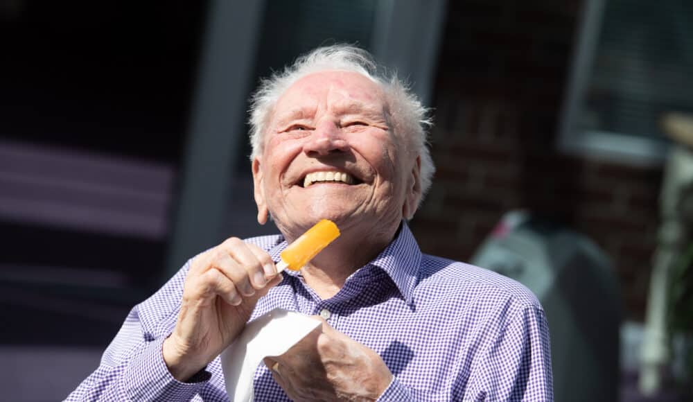 A male resident enjoying a delicious piece of ice cream, smiling as he takes a bite on a sunny day.