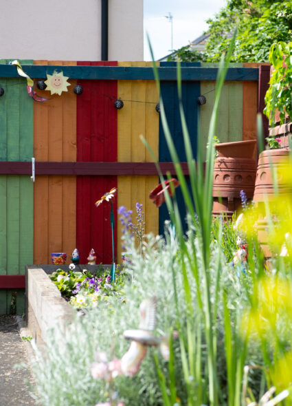 A vibrant fence stands in front of a blooming flower garden, showcasing a beautiful array of colors and nature's beauty.