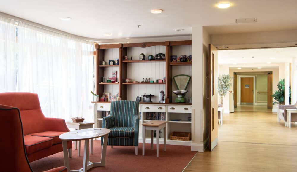 Communal lounge with comfy chairs and decorative shelves at James Terry Court care home.
