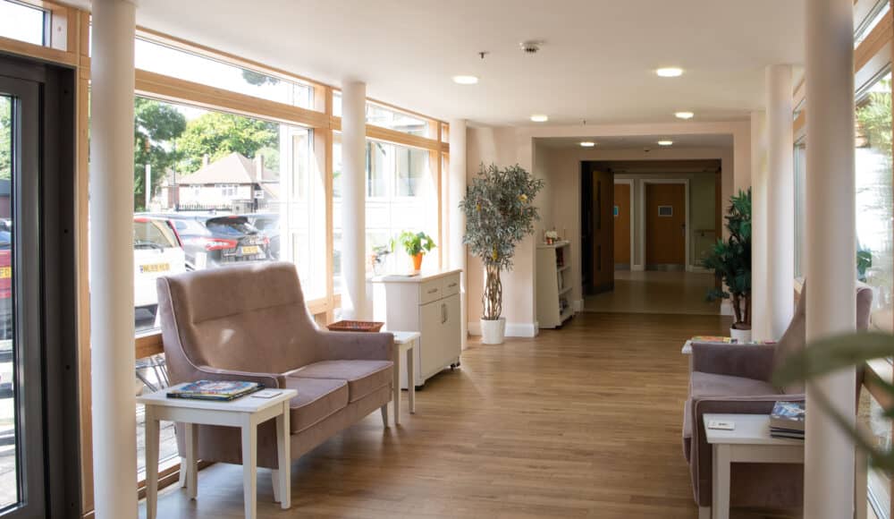 Communal seating and tables with flowers in an bright hallway at James Terry Court care home