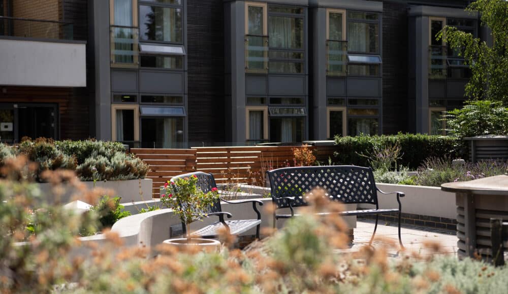 Outdoor seating area amongst garden flowers on the rooftop gardens of James Terry Court care home.