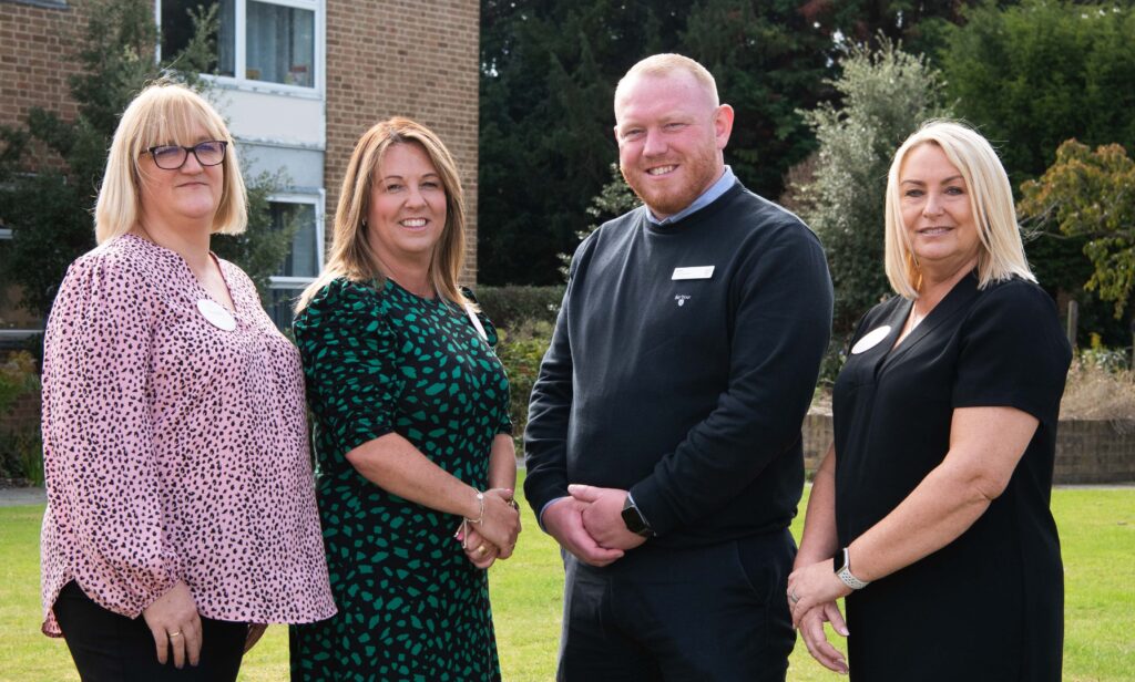 The Home Management Team stand together in front of a building, smiling and enjoying their time outdoors.