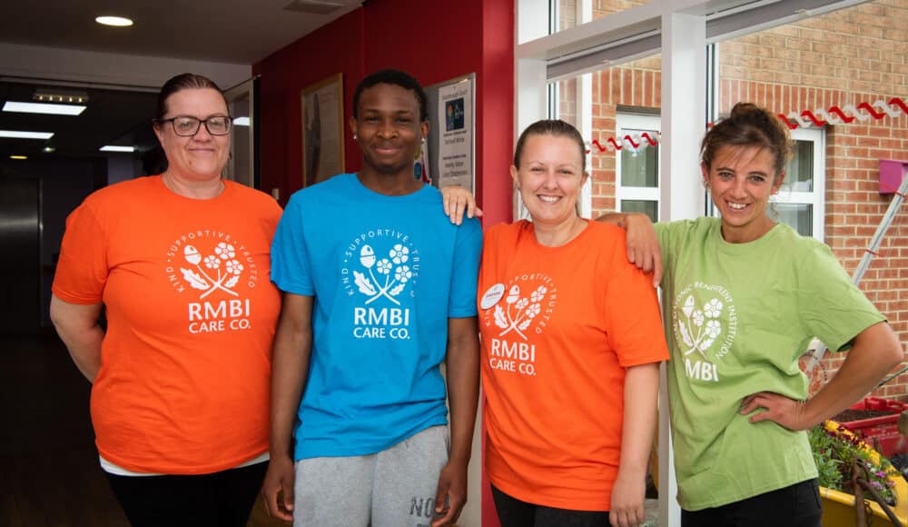 A group of staff wearing orange and blue shirts stands side by side, looking cheerful.