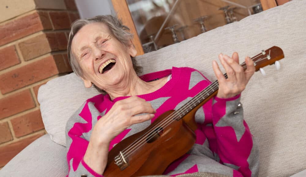 A resident joyfully playing a ukulele, immersed in music and creativity.