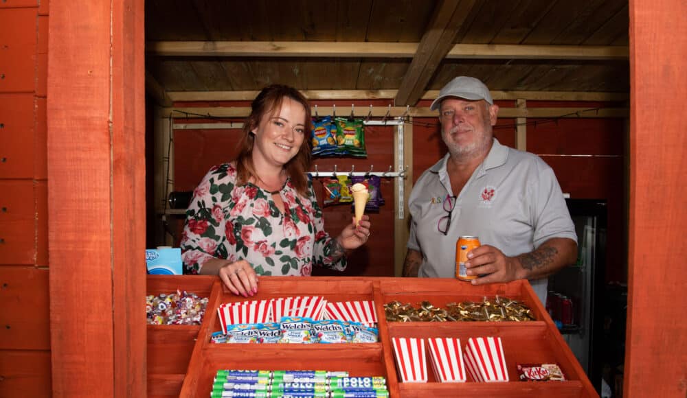 Staff members smile while standing in front of a colorful candy display filled with various sweets.