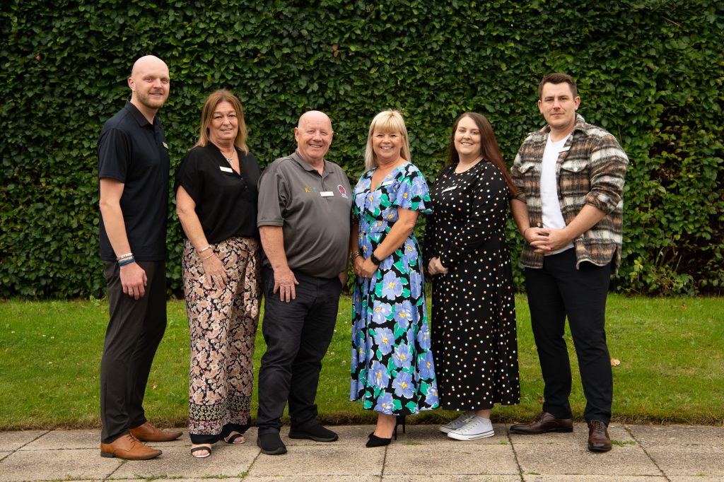 The Home Management Team stand together in front of a building, smiling and enjoying their time outdoors.