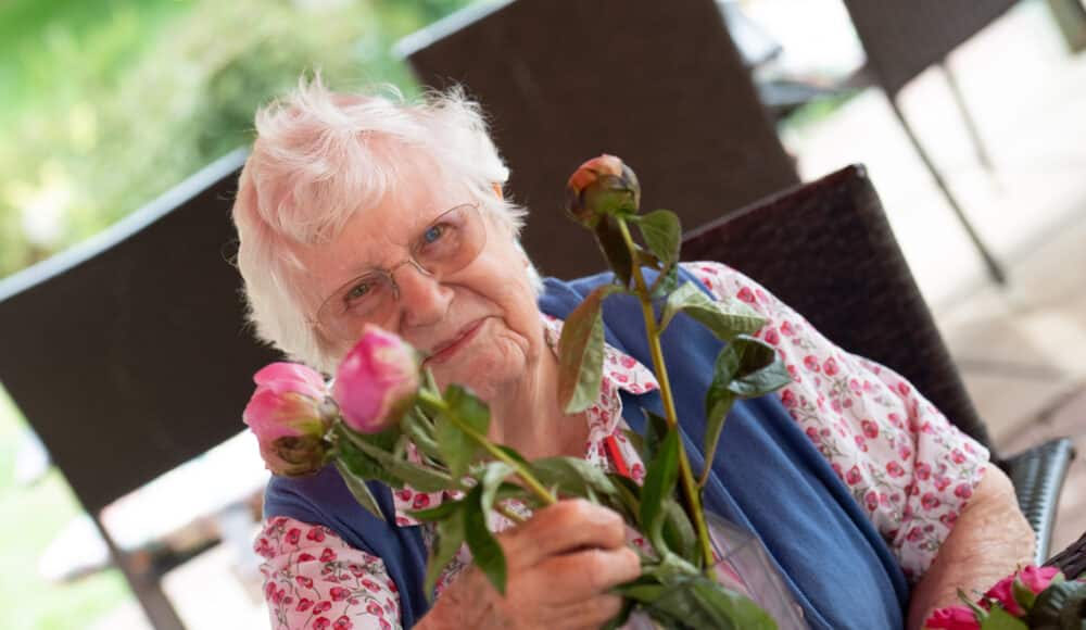 A female resident gently holds a vibrant flower, smiling softly as she admires its beauty.