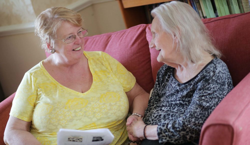 Resident and family member enjoying time together on a couch in the care home lounge room