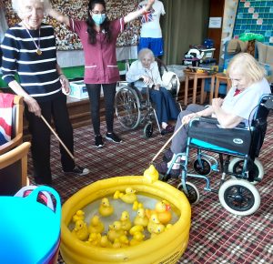 Residents Coral McGuillvray and Angela King engage in a hook a duck game while resident Irene Muggeridge and staff member Neus Amoros cheer on them.