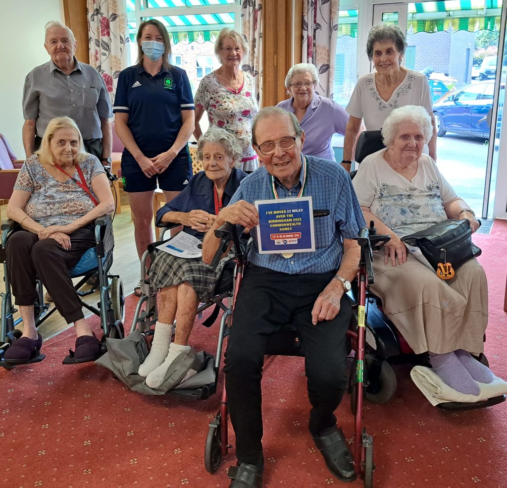 Resident Michael Holdstock shows a diploma certifying his achievement. Behind, Judo gold medal winner Megan Fletcher and Lord Harris Court residents smile at the camera. The residents attended a talk by Megan regarding her career in judo. All got to have a look and handle her gold medal.