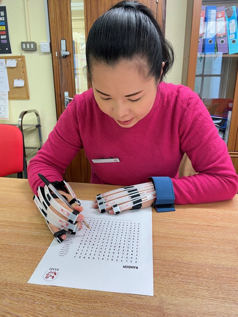 Staff member Lichai wears arthritis stimulation glove to complete a crossword. This shows how challenging activities can be if staff do not meet the residents’ abilities. 