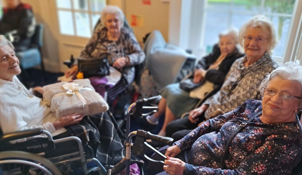 Residents Ann Green, Gladys Matthews, Margaret Sutherland and Angela Walmsley giving resident Joan a cosy blanket from everyone for her birthday.