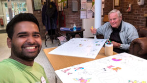 Resident Roy starts colouring the sign with Activities Coordinator Godwin.