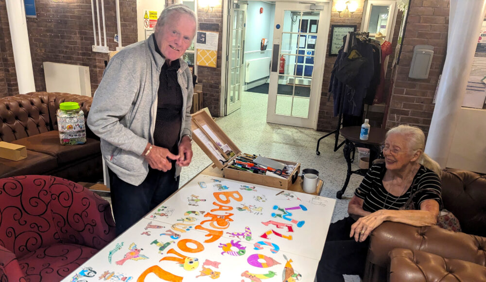 Residents Roy and Sylvia work together gleefully on the new handmade welcome sign at RMBI Care Co. Home Barford Court, in Hove.