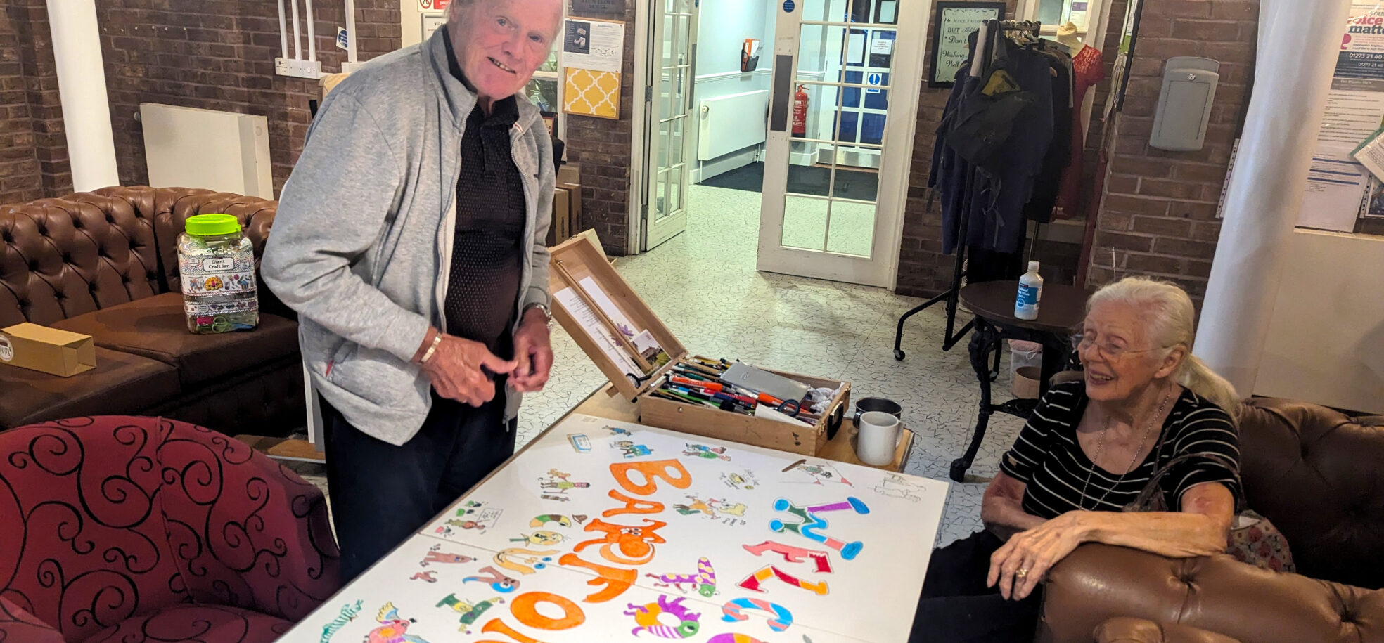 Residents Roy and Sylvia work together gleefully on the new handmade welcome sign at RMBI Care Co. Home Barford Court, in Hove.