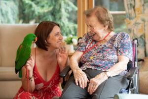 Resident Pat “ahoys” and winks at the parrot in true pirate spirit, accompanied by Senior Carer Veronika at James Terry Court, in South Croydon.