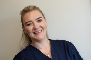 Emily wearing a nurse uniform, looks at the camera and smiles. 