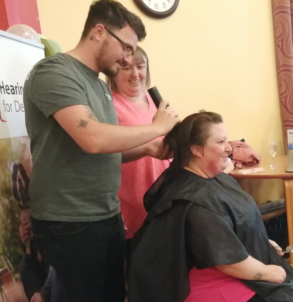 Staff members Panagiotis Celadaris in a green shirt, and Leigh Stephenson in a pink top, shaving Tracey Nichol’s locks at RMBI Care Co. Scarbrough Court, in Cramlington, Northumberland.