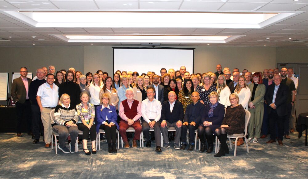 A large group of people pose for a photo in front of a projection screen in a conference room.