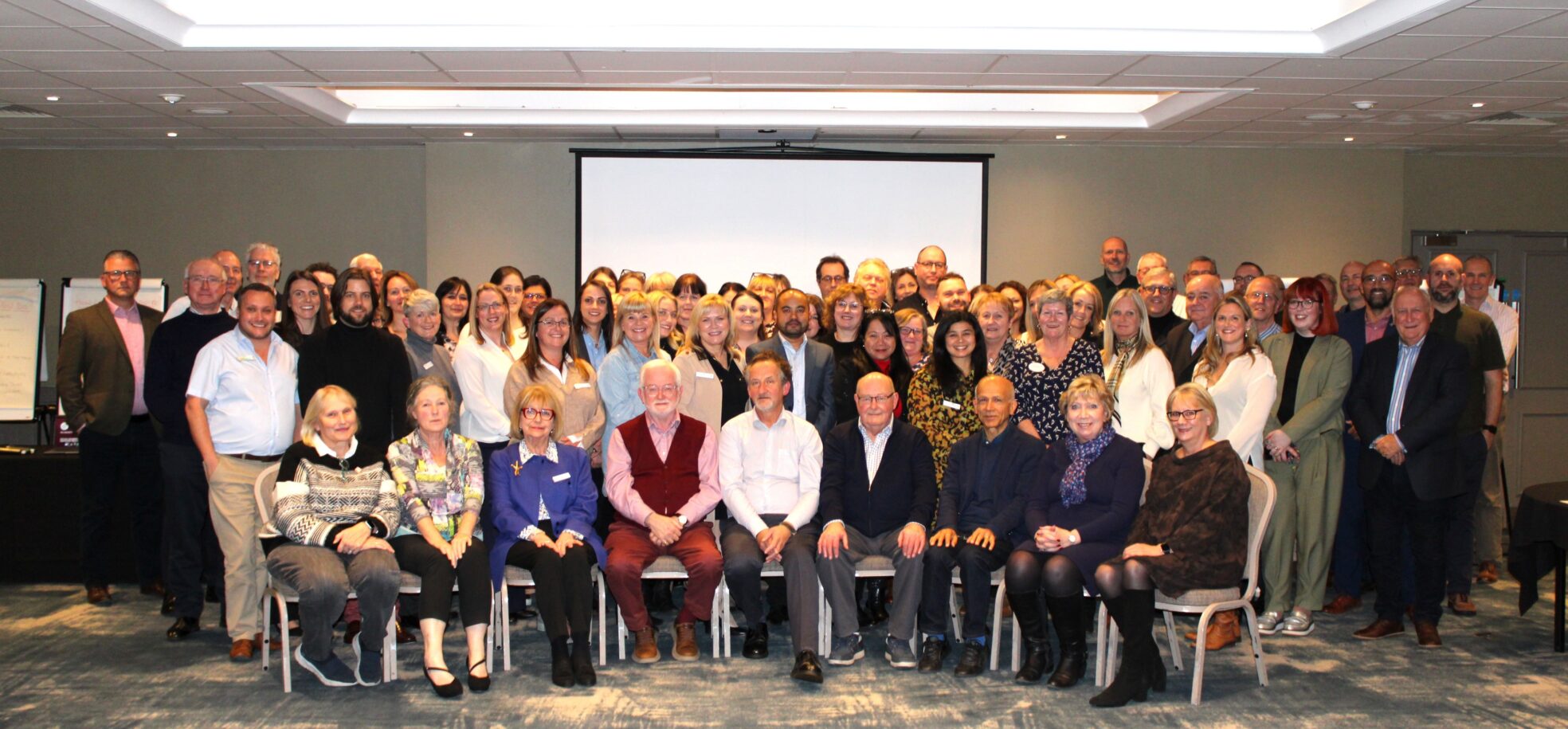 A large group of people pose for a photo in front of a projection screen in a conference room.