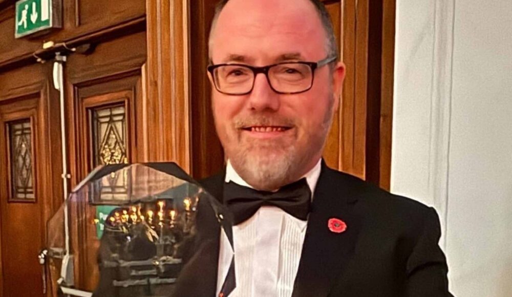 RMBI Care Co. Home The Tithebarn’s Care Home Manager, Simon Doherty in a black tuxedo, white shirt and glasses, holding his glass trophy at the Great British Care Awards ceremony for the North West region, in Manchester