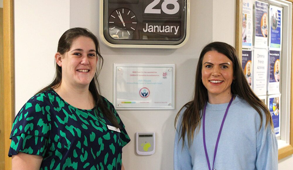 Dementia Lead Holly Langley (left) and Home Manager Abigail Cranston (right) proudly pose at either side of the new EMBRACE Dementia Accreditation plaque.