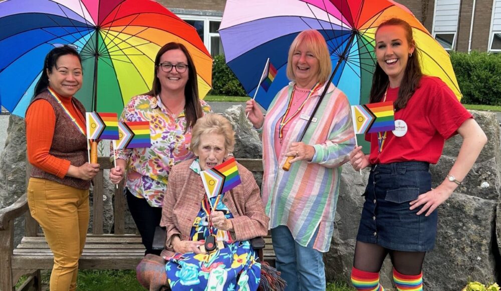 Resident Maureen celebrating Pride Month with the Home Management Team at RMBI Care Co. Home Queen Elizabeth Court, in Llandudno