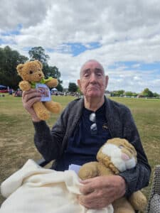 A male resident sitting with two teddy bears at the picnic.