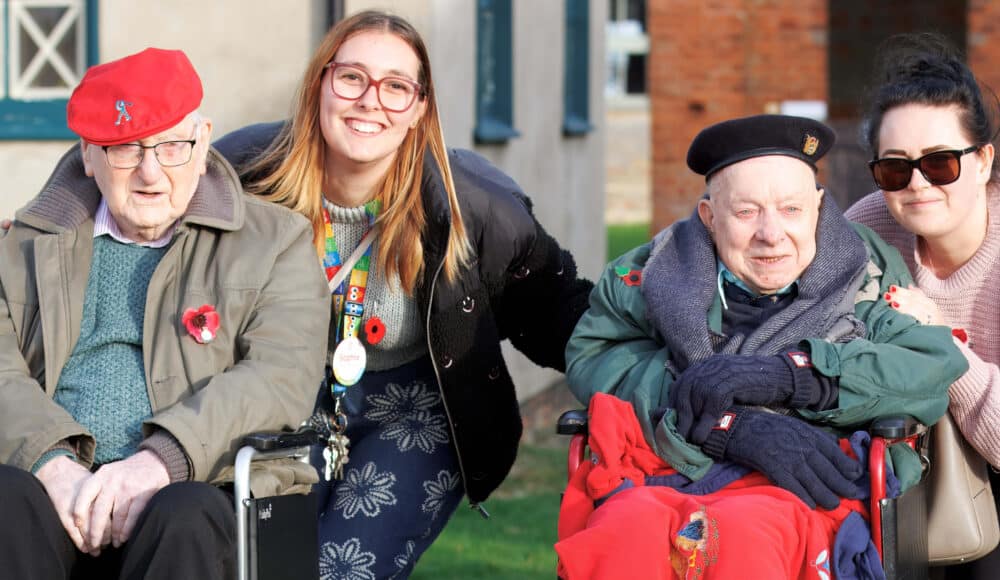 Two care home residents sitting in wheelchairs and two staff members standing next to them.