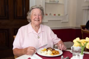 A smiling resident enjoys a tasty meal in a care home.