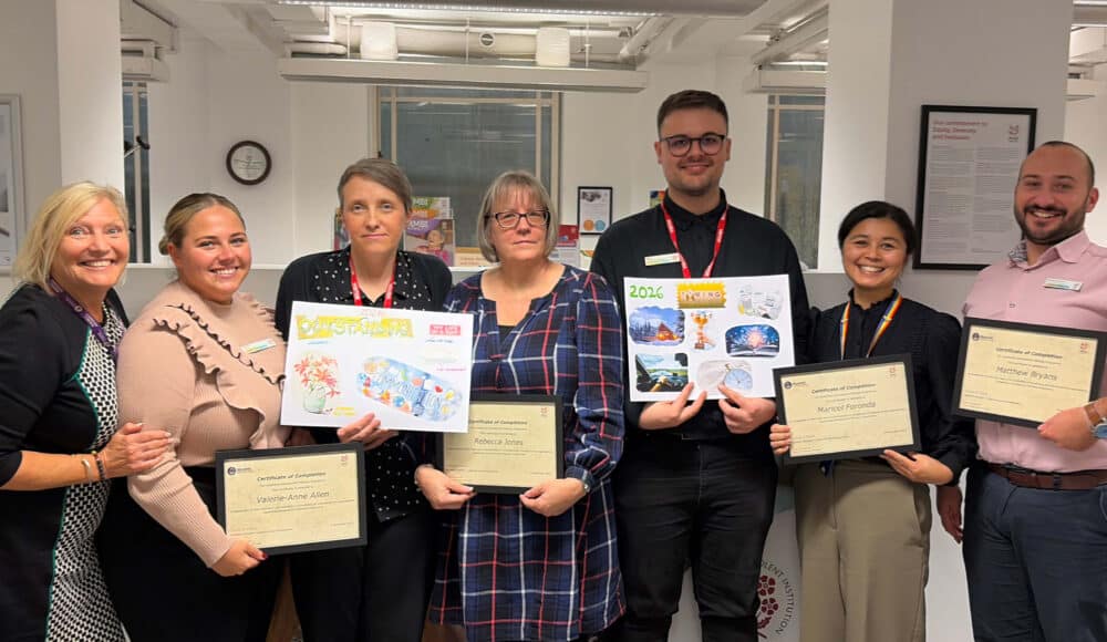 A group of care home staff members holding up their diplomas in an office.