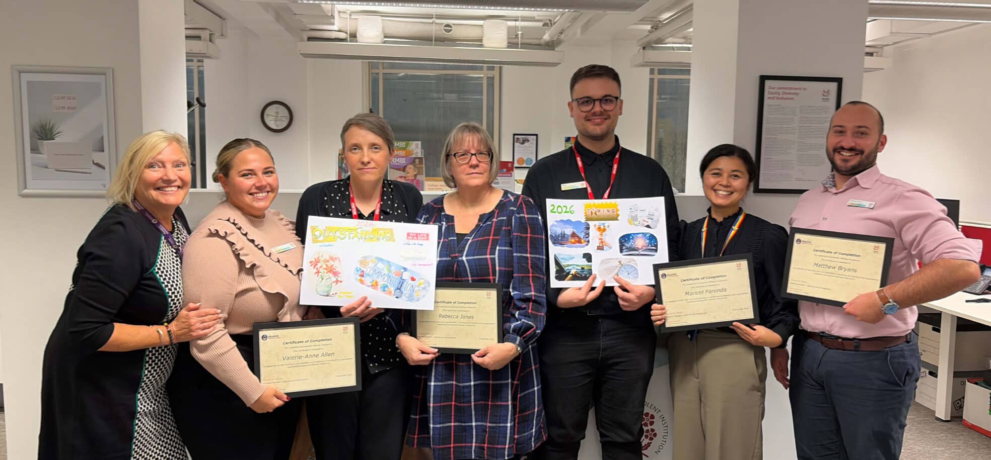 A group of care home staff members holding up their diplomas in an office.