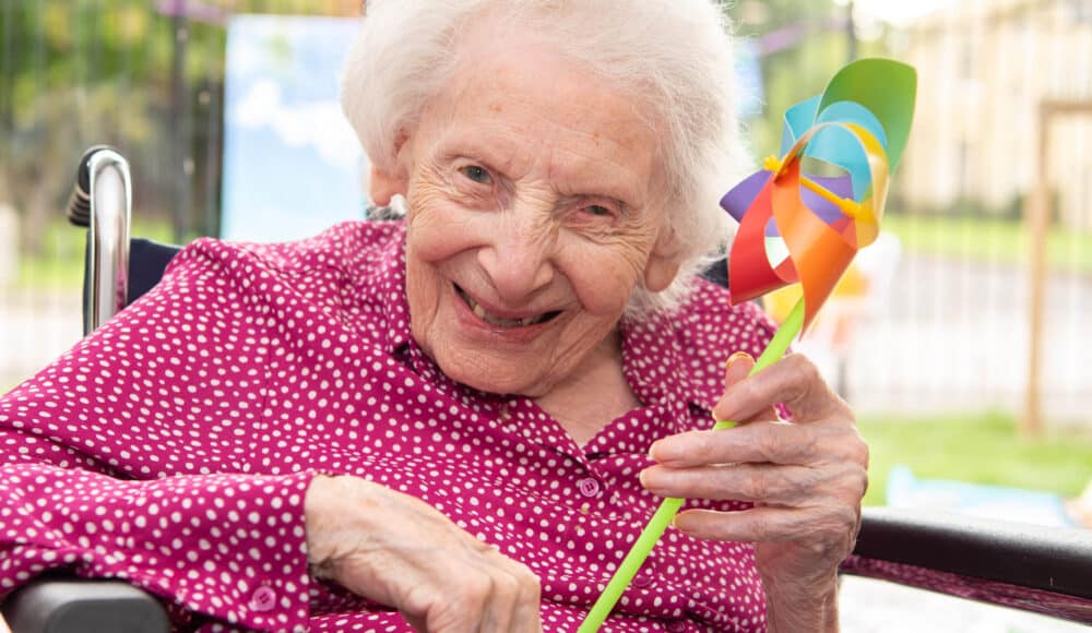 A care home resident smiling and holding her windmill toy.