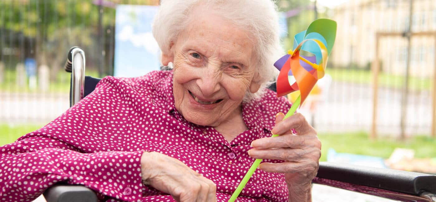 A care home resident smiling and holding her windmill toy.