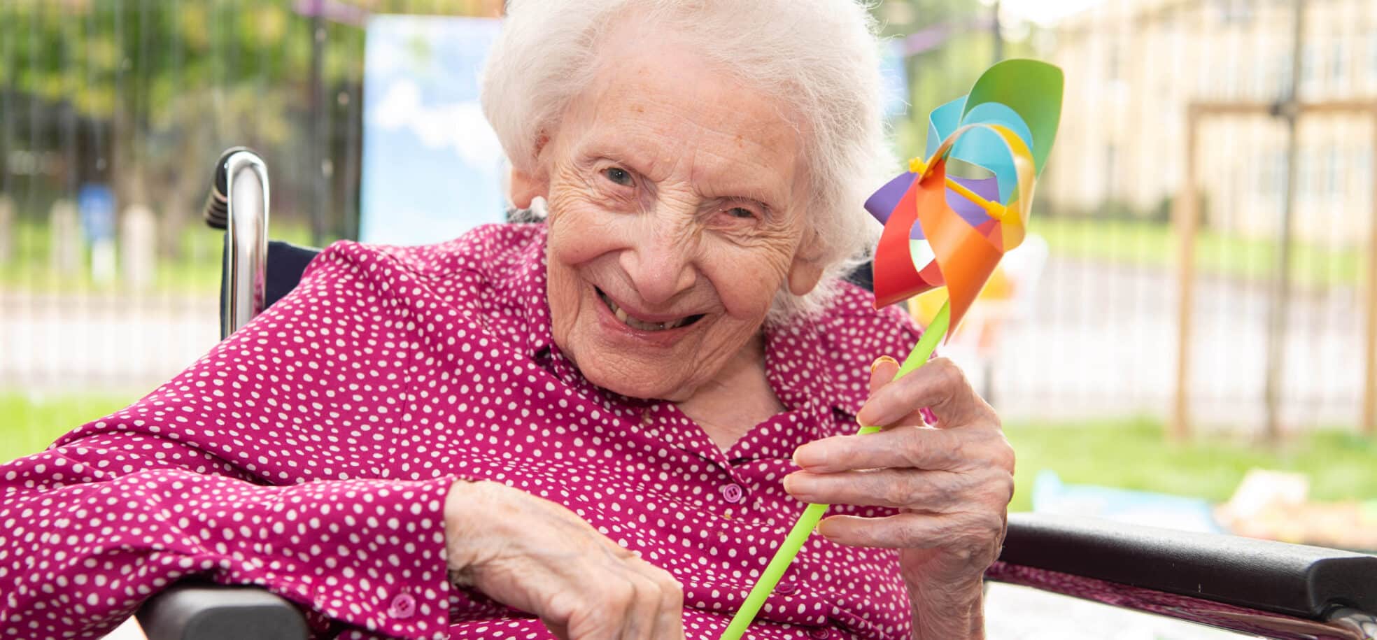 A care home resident smiling and holding her windmill toy.