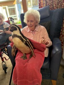 Resident plays with a penguin, sitting in her lap.