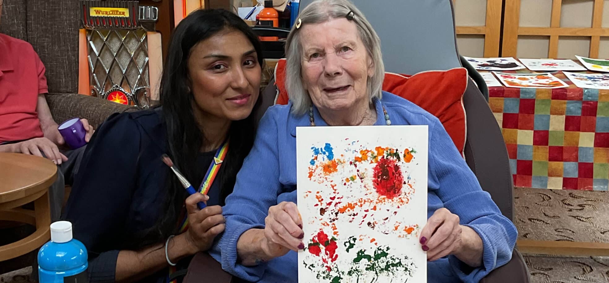 A care home resident holding up her creation, next to a staff member.
