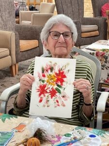 Resident Pamela smiles proudly while showing her painting.