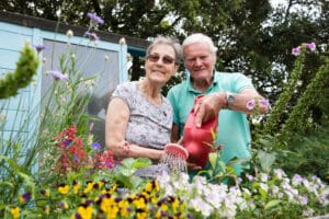 Two residents, a man and a woman, smile while watering a flowerbed.