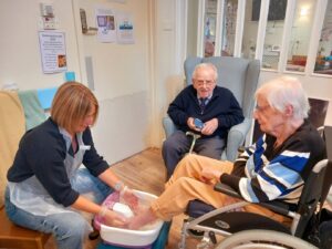 Two volunteers, a woman and a man, with a female resident. The female volunteer washes the resident's feet.