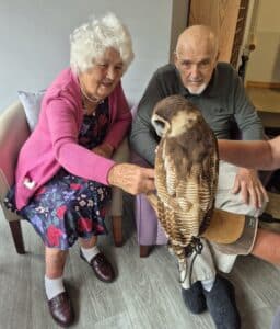 Two residents, a man and a woman, sitting and petting a friendly owl.